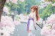 A woman in a white and purple outfit stands amidst cherry blossoms with a katana.