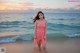 A woman in a pink dress standing on the beach.