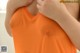 A woman in an orange tank top with her hands on her breasts.