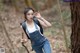 A woman in overalls and a backpack standing in the woods.