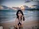 A woman in a bikini sitting in the water on a beach.