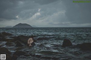 A person sitting on a rock in the middle of the ocean.