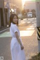 A woman in a white dress standing on the side of a road.