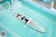 A woman in a black bathing suit laying on a surfboard in a pool.